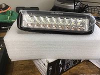 Alpena Hexfire Duel Work Light resting on white protective foam showing multiple LEDs and black frame with clear lens.