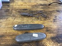 Two closed tin eyeglass cases and a pair of vintage scissors on a wooden surface