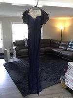 Full view of long blue gown hanging on a hanger, showing the entire length and silhouette in a living room.