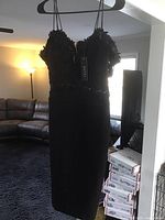 Full view of the black short ladies gown on a hanger, showing the fitted silhouette and overall length.