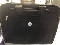 Front view of black Dell computer bag showing the Dell logo on a circular badge in the center front pocket. The bag has two carrying handles and a zippered front compartment.
