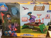 Front view of the boxed Dino Obstacle Course set showcasing the character and dinosaur figures and playset components like the spinning barrel and trapdoor.