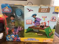 Photo shows the boxed Dino Ranch obstacle course play set including character and dinosaur figures and the interactive obstacle course with trapdoor and spinning barrel features.