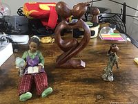 Overview of all three items on a table: a figurine, a wooden abstract carving, and a metal carving.
