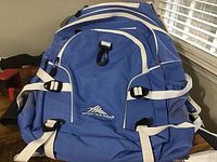 Front view of blue High Sierra backpack showing multiple compartments, white straps, mesh side pockets, and logo on front.