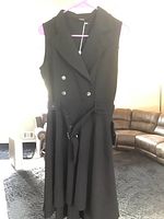 Front view of black sleeveless double-breasted dress on hanger with silver buttons and belt visible.