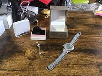 Overview photo showing silver-tone ladies wristwatch, belly ring, and packaging boxes on wooden surface.