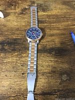 Mens Fossil wristwatch with round dial showing brand on face and two-tone metal band laid flat on wooden surface with pen nearby.