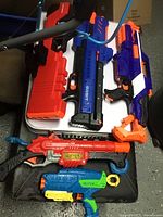 Five Nerf blasters arranged on a white table and black surface showing colors, shapes and details of each toy gun.