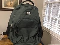 Full front view of green Nicks Club backpack on wooden surface.