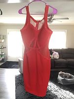 Front view of the red dress on a hanger showing the mesh and bead design, sleeveless style, and overall shape.