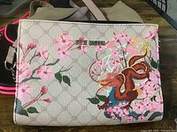 Steve Madden purse showing beige background with signature pattern and colorful floral and dragon design