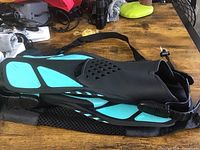 Side view of one swim fin showing black and turquoise coloring with ventilation holes and adjustable strap.