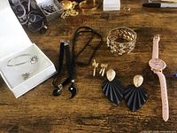 Overview photo of women's jewelry lot featuring multiple pairs of earrings, bracelets, necklaces on a tabletop, and a pink wristwatch.