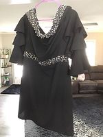 Full front view of black dress blouse size 2X with white bead and pearl embellishments on neckline and waist, showing layered flutter sleeves and draped neckline.