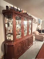 Full view of antique wooden china cabinet showing polished dark wood, glass display doors, and curved top design with shelves inside.