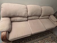Front angle view of the beige cushioned couch showing three seat cushions, cushioned back ends, and wooden armrest base on the left side.