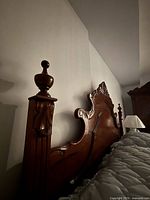 Side view showing the ornate carved finial and scrollwork on the headboard of the wood bedframe.