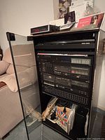 Full view of media cabinet with stereo components and some paper items on top, located next to a beige couch.