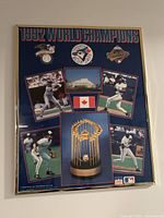 Straight on view of framed Blue Jays 1992 World Champions poster showing players, logos, trophy and Canadian flag.