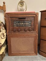Front view of vintage wooden radio console showing the tuning dial, four control knobs, and speaker grille.