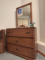 Frontal view of wood vanity with large rectangular mirror and three drawers.