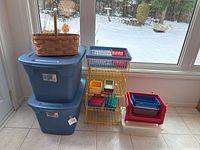Photo showing two large blue plastic tote bins stacked and wooden baskets and wire metal shelving with plastic baskets on the shelves