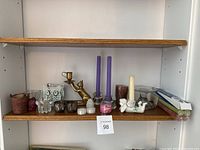 Shelf view showing various candle holders and candles including brass cat holder, cherub holder, glass owl, purple tapered candles, tealights