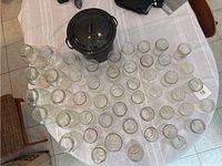Overview of black canning pot with lid surrounded by various clear glass jars on a white tablecloth.