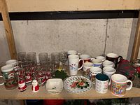 Full view of vintage Christmas-themed glassware, mugs, Lenox candy dishes, a Christmas keepsake plate, and Santa Claus salt and pepper shakers arranged on a table.