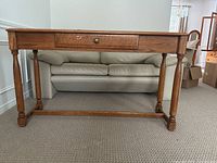 Front view of the oak console table showing turned legs, drawer with brass knob, and stretcher bars.