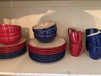Full view of red and blue Denby plates, bowls, and mugs arranged on shelf