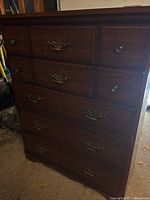 Front view of the tall wood dresser showing five drawers with metal handles and overall structure.
