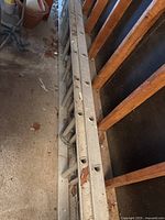 Folded extendible aluminum ladder leaning against a wooden wall in a garage, showing overall structure and condition.