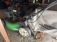 Side view of green LawnBoy gas lawnmower with mulch bag and plastic wheels, some leaves on wheels and bag.