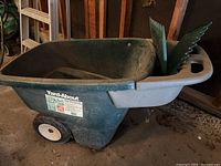 Full side view of the green Yard-About lawn cart with storage tray and two wide white wheels on a concrete floor.