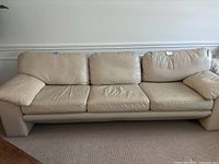 Front view of beige leather three-seater sofa on carpet against wall