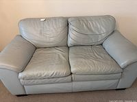 Front view of light blue leather loveseat with removable seat and back cushions shown in good, stable condition with no visible rips.