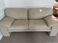 Front view of beige leather two-seater sofa showing two seat cushions and two back cushions with wide armrests.