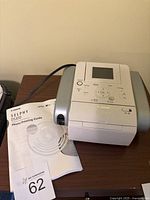 Canon Selphy DS810 photo printer with photo printing guide manual beside it on a table, showing top and front control panel clearly.