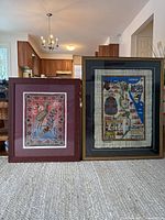 Two framed pictures side by side on the floor, showing Egyptian papyrus artwork on the right and Aboriginal art on the left.