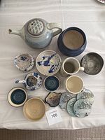 All items arranged on a cloth, showing teapot, mugs, bowls, coasters, and small decorative dish