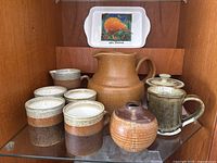 Photo showing full set of pottery including large jug, preserve pot, creamer, vase, mugs, and a souvenir tray