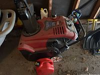 Snowblower positioned in garage with red gas can in front