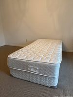 Twin mattress on top of matching boxspring set in carpeted room against plain wall.