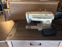 Singer 533 sewing machine on wooden work table from side view showing sewing machine front and foot pedal