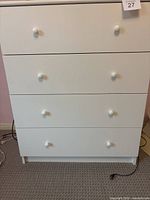 Front view of white dresser showing four drawers, each with two white round knobs.