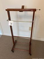 Front angle view of the Italian vintage wood valet stand showing wood finish, metal bars, leather strap, and base.