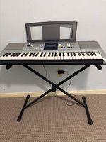 Front view of Yamaha electronic keyboard on X-style metal stand against wall, plugged in