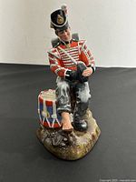 Front view of Royal Doulton Drummer Boy figurine showing soldier in red uniform seated with one boot off, next to a drum.